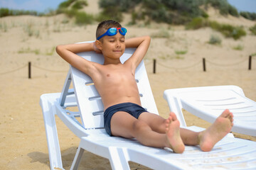 Young guy in swimming glasses is sunbathing on a sunbed on the sea beach.