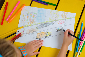 Child draws a pencil drawing of the city, cars and air pollution. Top view.