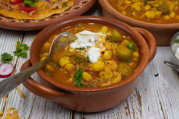 Vegetarian okra pozole and corn quesadillas in traditional Mexican clay dishes, wooden table.