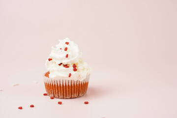 One homemade chocolate muffin with white creamy frosting and heart-shared red and white sugar decoration on marble board on pink surface