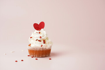 One homemade chocolate muffin with white creamy frosting and heart-shared red and white sugar decoration on marble board on pink surface
