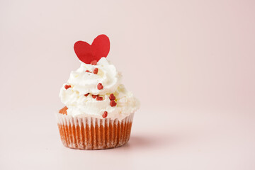 One homemade chocolate muffin with white creamy frosting and heart-shared red and white sugar decoration on marble board on pink surface