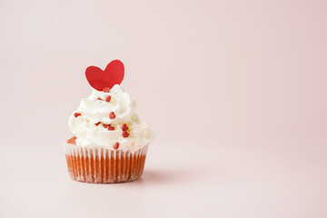 One homemade chocolate muffin with white creamy frosting and heart-shared red and white sugar decoration on marble board on pink surface