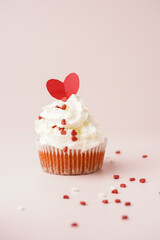 One homemade chocolate muffin with white creamy frosting and heart-shared red and white sugar decoration on marble board on pink surface