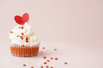 One homemade chocolate muffin with white creamy frosting and heart-shared red and white sugar decoration on marble board on pink surface