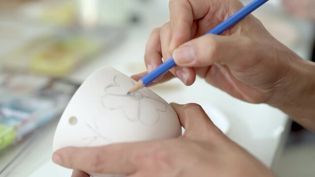 Asian Lgbtq guy design stylish pattern for painting self-made pottery mug with friends. Happy man enjoy leisure activity handicraft hobbies ceramic sculpture painting workshop at pottery studio