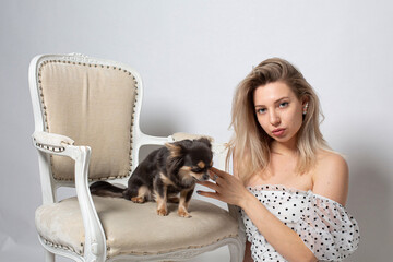 Woman with blonde hair and white skin isolated on grey with small black dog in chair