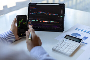 An investor is looking at stock charts on mobile phones and tablets, he is a stock investor, he trades stocks by analyzing the charts and using indicators to enter trades. Stock investment idea.