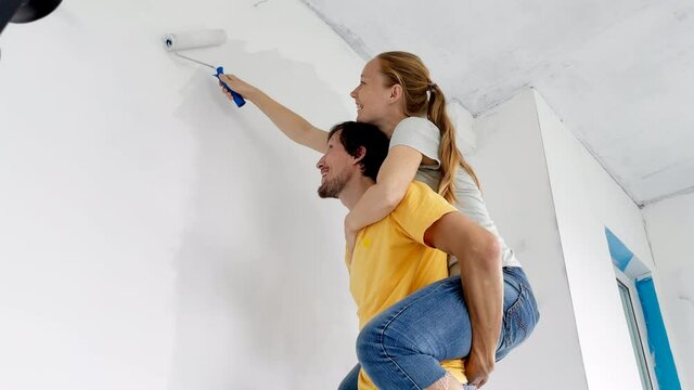 A happy man and woman paint the wall using a roller painter. They are renovating their apartment. DIY home renovation concept. Family time. Slowmotion shot
