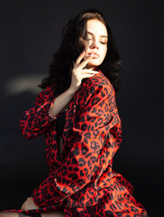 Young dark haired woman with white skin on dark background in leopard print clothes and fingers on her lips