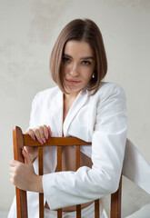 Portrait of white european woman with bob cut sitting on chair in white business suit