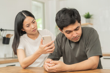 Obraz na płótnie Canvas Infidelity, suspicion asian young couple love fight relationship, wife holding cellphone, smartphone cheating on phone, scolding husband about mistrust, distrust and jealousy when sitting at home.