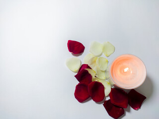 valentine's day decoration with scented candle and rose petals of red, yellow, white colors in white background.