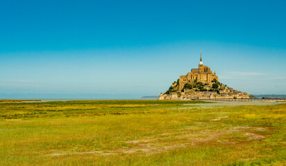 Stunning view of famous Le Mont Saint Michel tidal island on a bright sunny day with empty green...