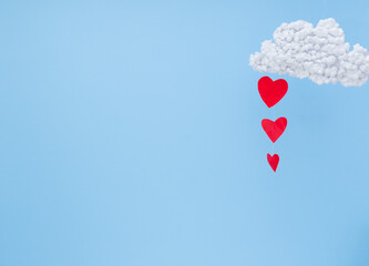Fototapeta na wymiar White clouds and red paper hearts in the form of rain on a blue background. 