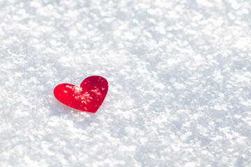 A red heart lies in the snow on a sunny day, a place for text