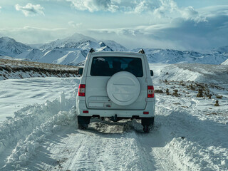 A white SUV makes its way through a snowy road in the mountains.