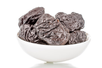 Several organic sweet prunes on a white ceramic saucer, macro, isolated on white.