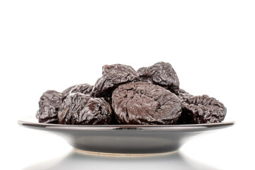 Several organic sweet prunes on a black saucer, macro, isolated on white.