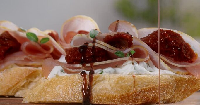 Balsamic is poured in slow motion to the bruschette with ham and dried tomatoes, 4k 60fps Prores
