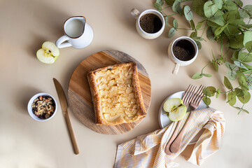 Top view of table setting  with homemade apple pie, coffee cups ,milk and nuts on beige backgroun with green plant.