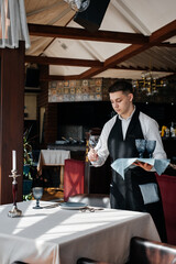 A young male waiter in a stylish uniform is engaged in serving the table in a beautiful gourmet restaurant. A high-level restaurant. Table service in the restaurant.