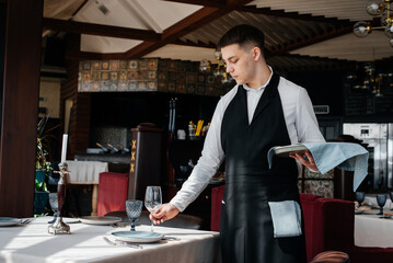 A young male waiter in a stylish uniform is engaged in serving the table in a beautiful gourmet restaurant. A high-level restaurant. Table service in the restaurant.