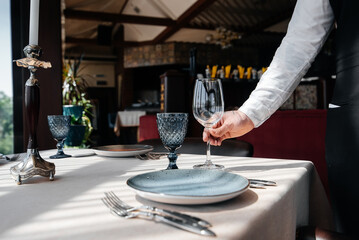 A young waiter in a stylish uniform is engaged in serving the table in a beautiful gourmet restaurant close-up. Table service in the restaurant.