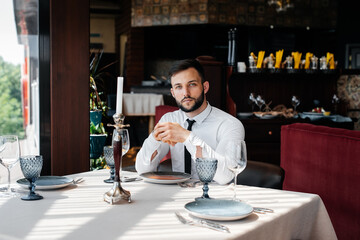 A young bearded male businessman is sitting at a table in a fine restaurant and waiting for his order. Customer service in the catering.