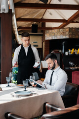 A young businessman in a fine restaurant examines the menu and makes an order to a young waiter in a stylish apron. Customer service. Table service in the restaurant.