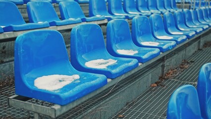 Row of Empty Plastic Seats on Sports Stadium Tribune Covered in Snow on Cold Winter Day During Off...