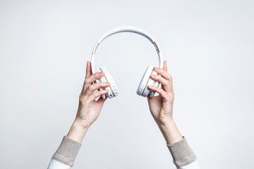 Female hands holding large white headphones on a light background.