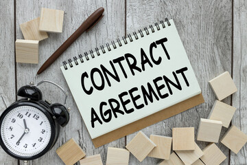 contract agreement block action text with spring on wooden background near alarm clock and wooden blocks