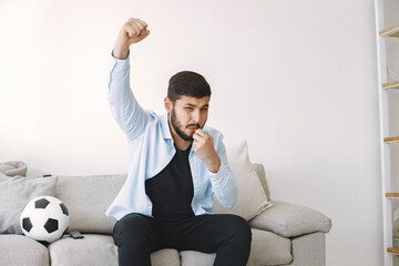 Brunette guy sitting on a coach and watching football at home