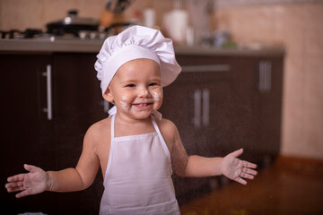 
a small child dressed as a cook claps his hands and scatters wheat flour