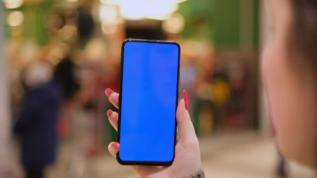 young woman holding a phone with chroma key on the background of a supermarket. The girl is holding a smartphone with a green screen and in the mall. Business woman working on smartphone surfing the
