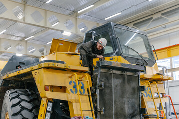 A mechanic repairs a dump truck in an industrial garage.