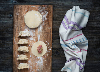 Gyoza in making: wooden board with gyoza skin circles and gyoza dumplings, towel on the side.