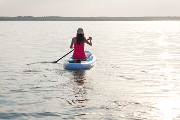 Fototapeta na wymiar Sporty woman sitting on Paddle Board rowing a view from the back. SUP. 