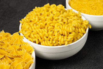 Close up of several types of dry pasta in a plate on dark background