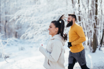 Happy young couple jogging outside in forest in a cold snow weather.