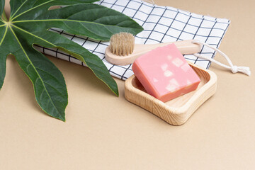 Handmade pink soap and wooden brush on beige backgound. Set for morning facial care routine