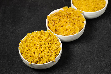 Close up of several types of dry pasta in a plate on dark background