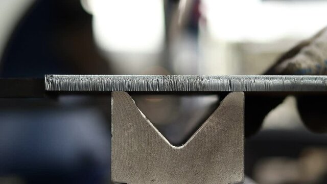 Work in heavy industry. A bending machine operator bends a thick, rusty sheet of metal on an old but powerful machine. Worker works at a metalworking plant