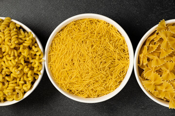 Close up of several types of dry pasta in a plate on dark background