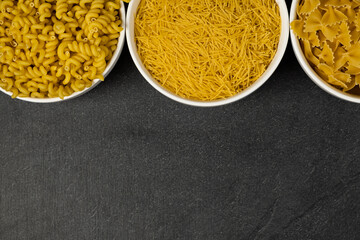 Close up of several types of dry pasta in a plate on dark background