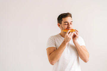 Portrait of happy young man with enjoying eating delicious slice of pizza, with closed eyes from...