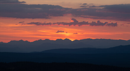 Silhouettes of mointains against the warm sunset that lights up the clouds