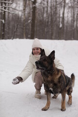 a girl in white hugs a dog against the background of snow and forest