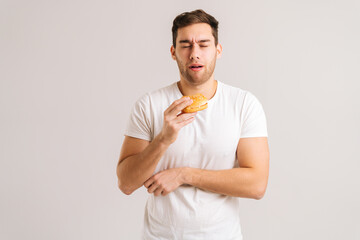 Portrait of hungry young man eating bad burger and suffering stomach ache, feeling nausea, food...